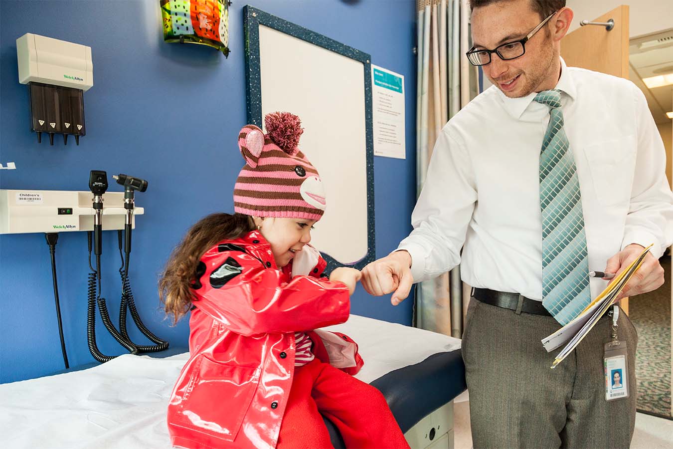 A doctor greets a child with a fist bump in an exam room.