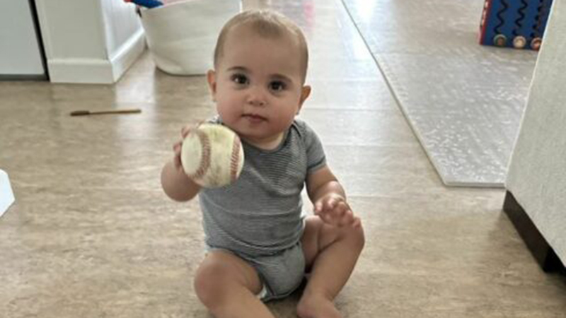 an infant holds up a baseball