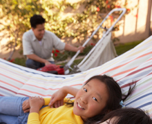 A child in a hammock with father and lawnmower