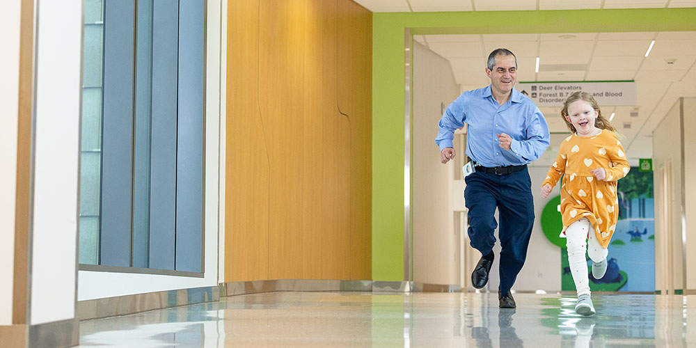 A man runs with a girl down a Seattle Children's hallway