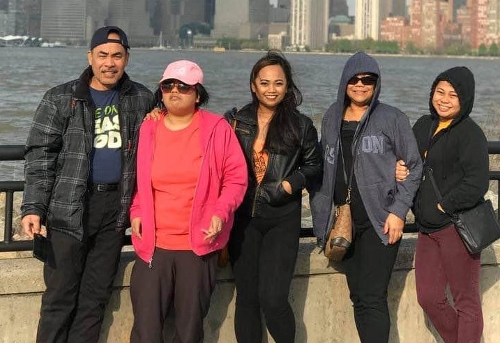 A family of five poses together near a black railing in front of a body a water