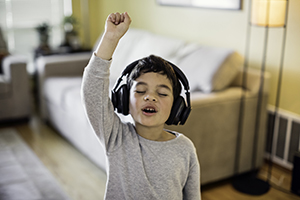 A boy wearing black headphones raises his right arm while listening to music