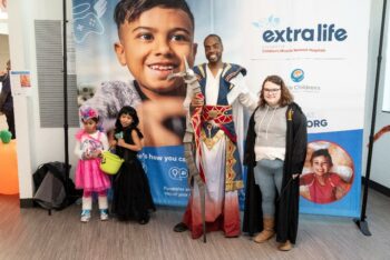 two adults and two children pose in front of a Extra Life branded step and repeat background
