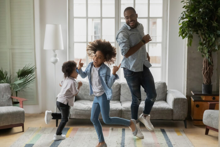 A father and his young daughter and son dancing happily in a living room