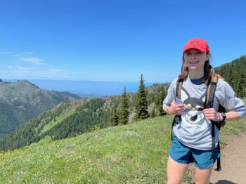 A teen girl smiles at the camera while on a hike where you can see how far she has come