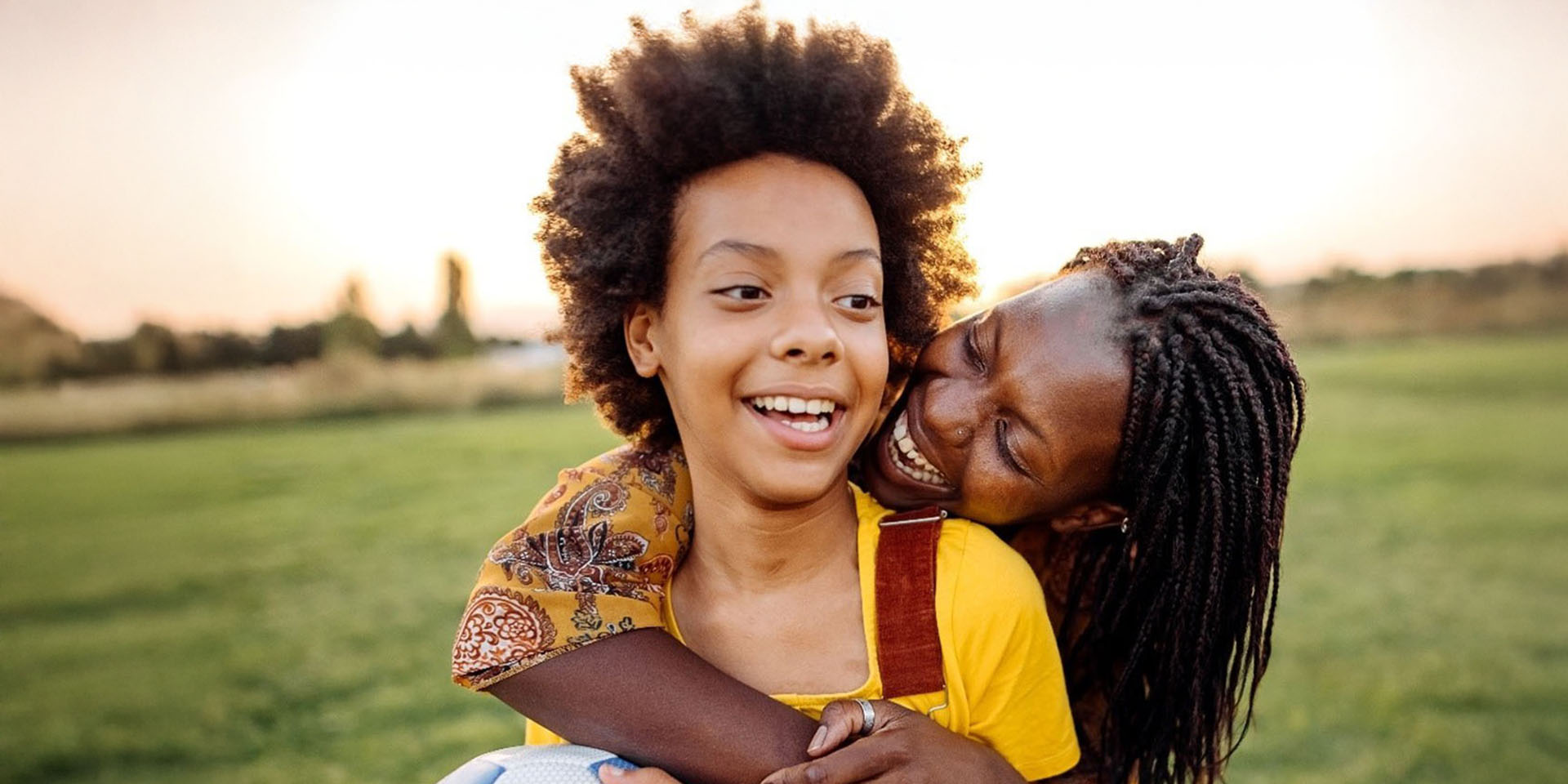 A smiling girl is wrapped in a hug from behind by a woman