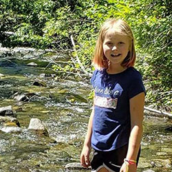 A school aged girl smiles and poses on a streambed.