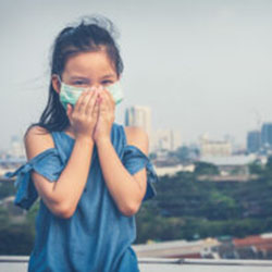 A girl stands outside and holds a mask to her nose