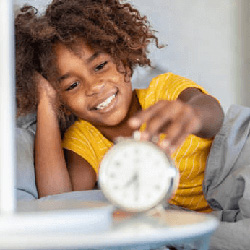 A child in bed reaches for an alarm clock