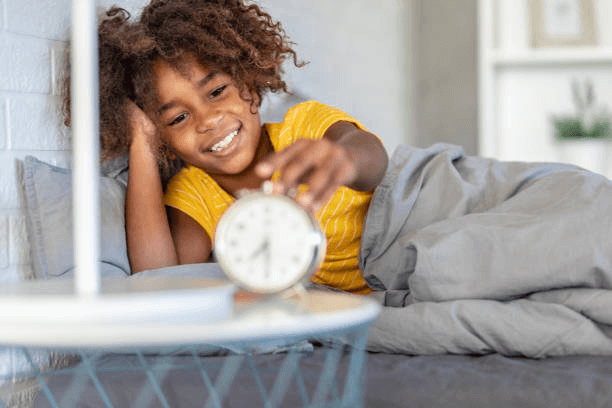 A kid in bed with an alarm clock