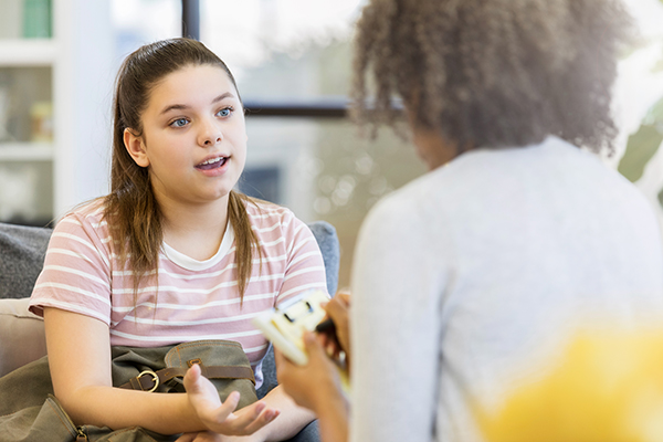 a teen girl sits on the couch while talking to a woman she is facing