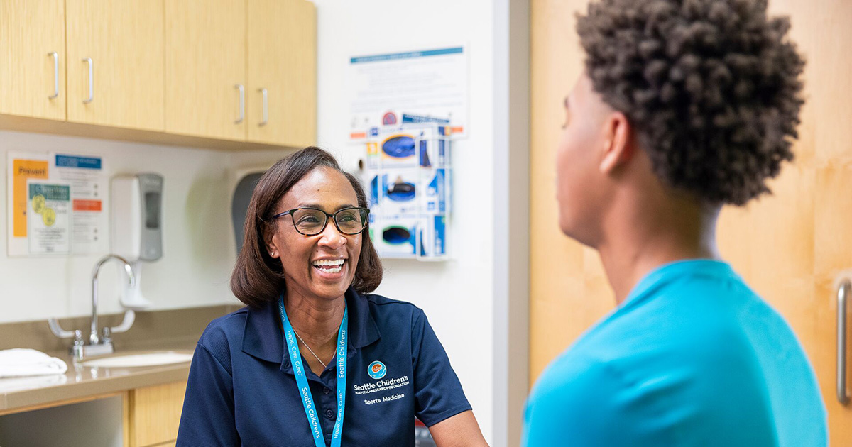 A female Seattle Children's doctor smiles as she interacts with her patient in an exam room