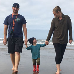 A boy holds hands with his mother and father on a beach