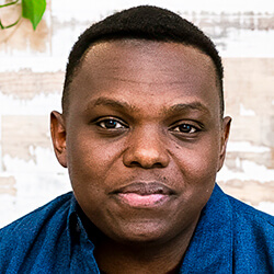 A man wearing a dark blue shirt and standing in front of a light-colored, textured wall