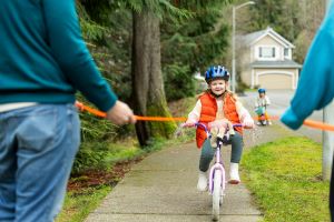 A little girl rides her bike down a sidewalk wearing an blue helmet