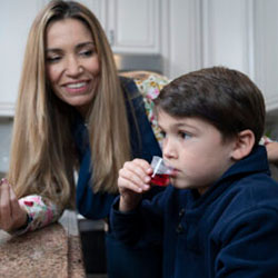 A boy sips medicine as his mother watches