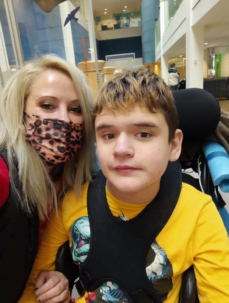 A teen boy in a wheel chair with his mom leaning in for the photo