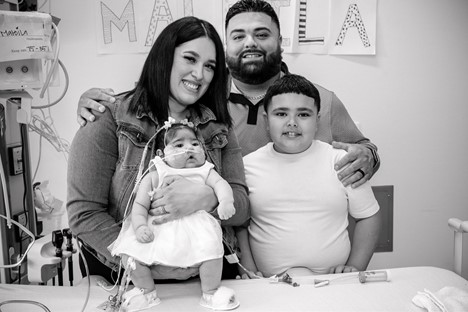 A family smiles at the camera from their baby girl's hospital room