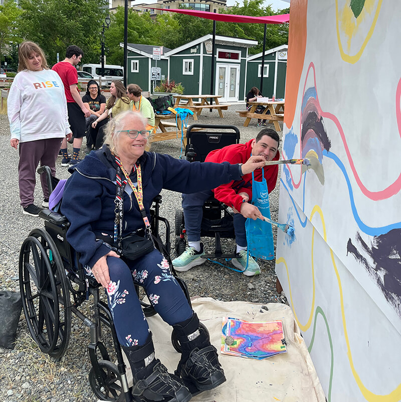 Two participants in wheelchairs painting a section of the mural