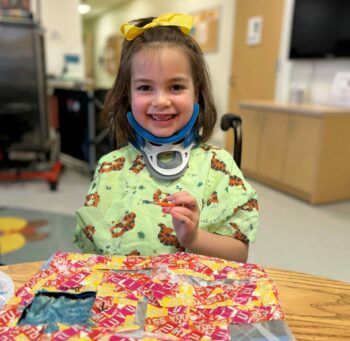A smiling, little girl with a yellow bow in her hair is working on her art for the spacesuit