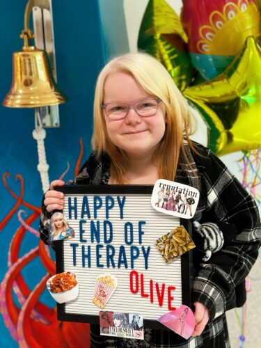 Olive Ray poses with a sign that says Happy End of Therapy Olive