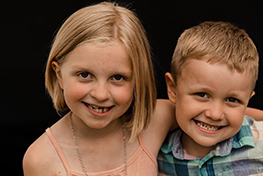 A young girl and a her younger brother smile at the camera