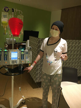 A teen stands with her IV pole that is delivering her chemotherapy
