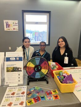 three women at a table with prizes and a wheel to spin on it