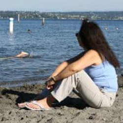 A woman sits on a sandy beach and looks at the water