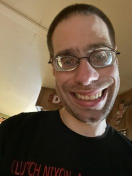 A closeup photo of a young man wearing glasses smiling at the camera