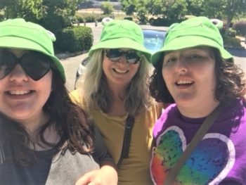 Three women wearing green frog hats smile at the camera