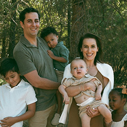 A family of five pose together wearing neutral colors outside for a photo 