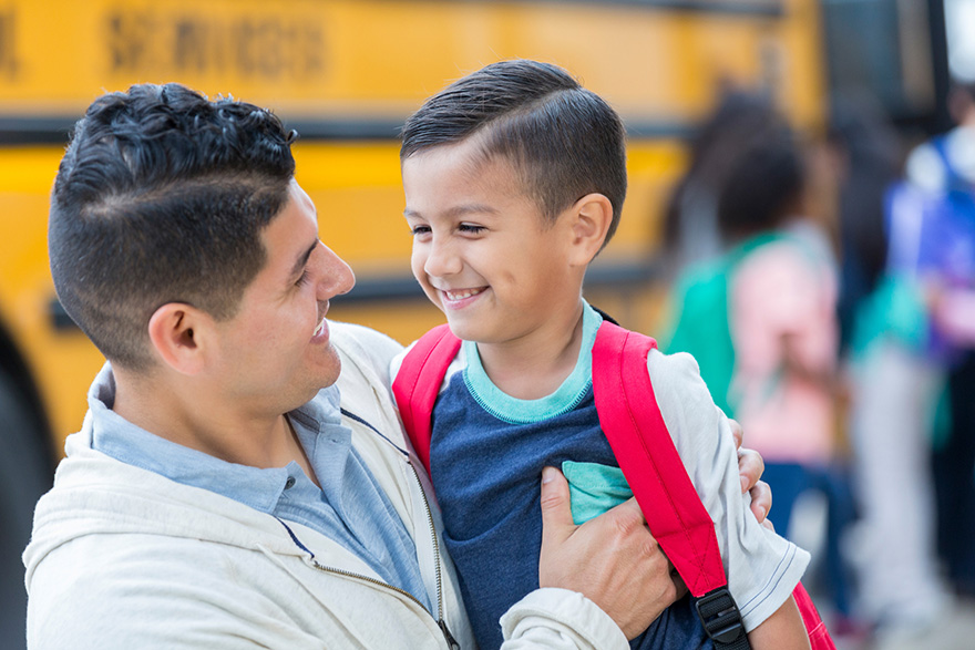 A father holds his son in front of a school bus