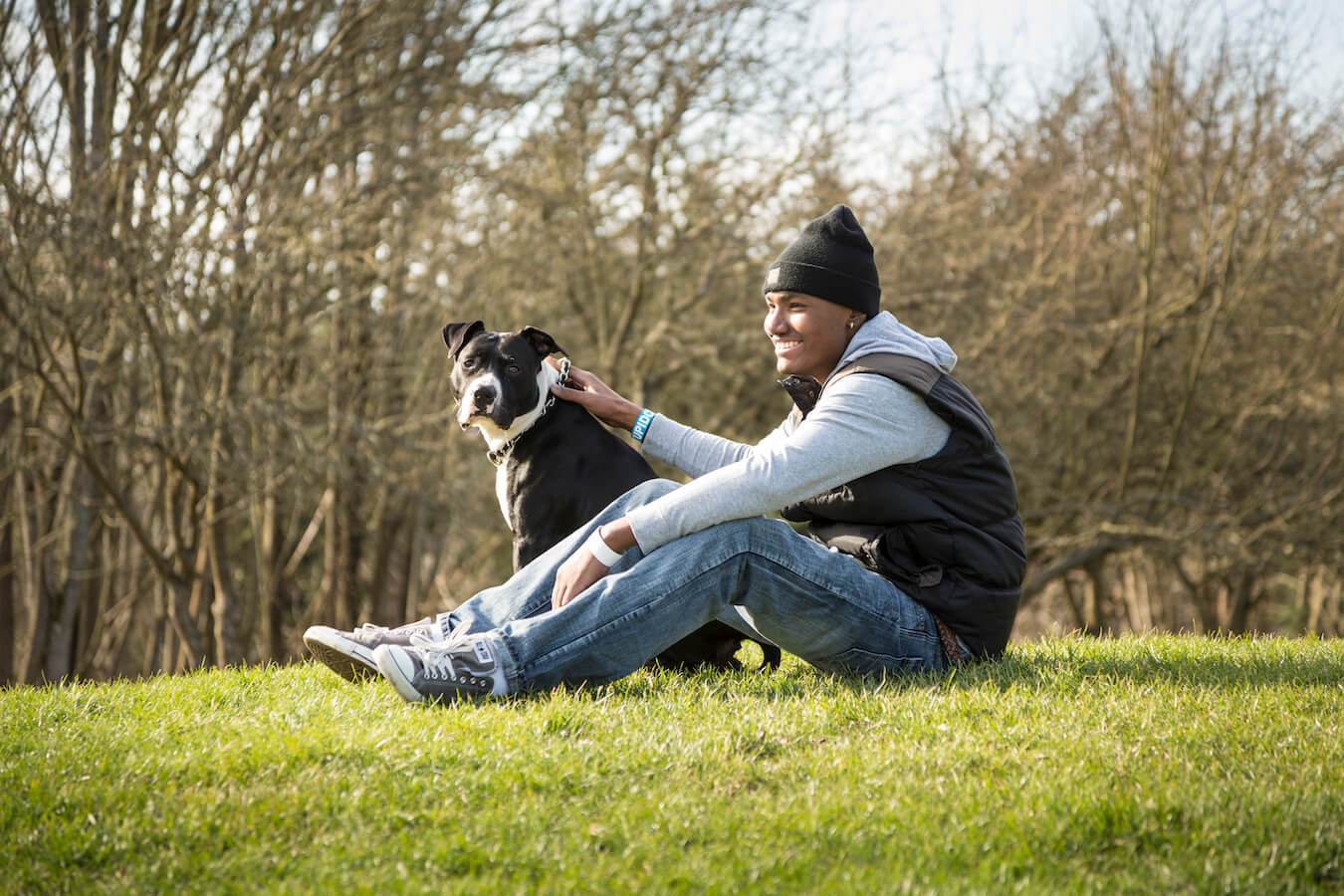 AYA cancer survivor sits on a green lawn petting a dog