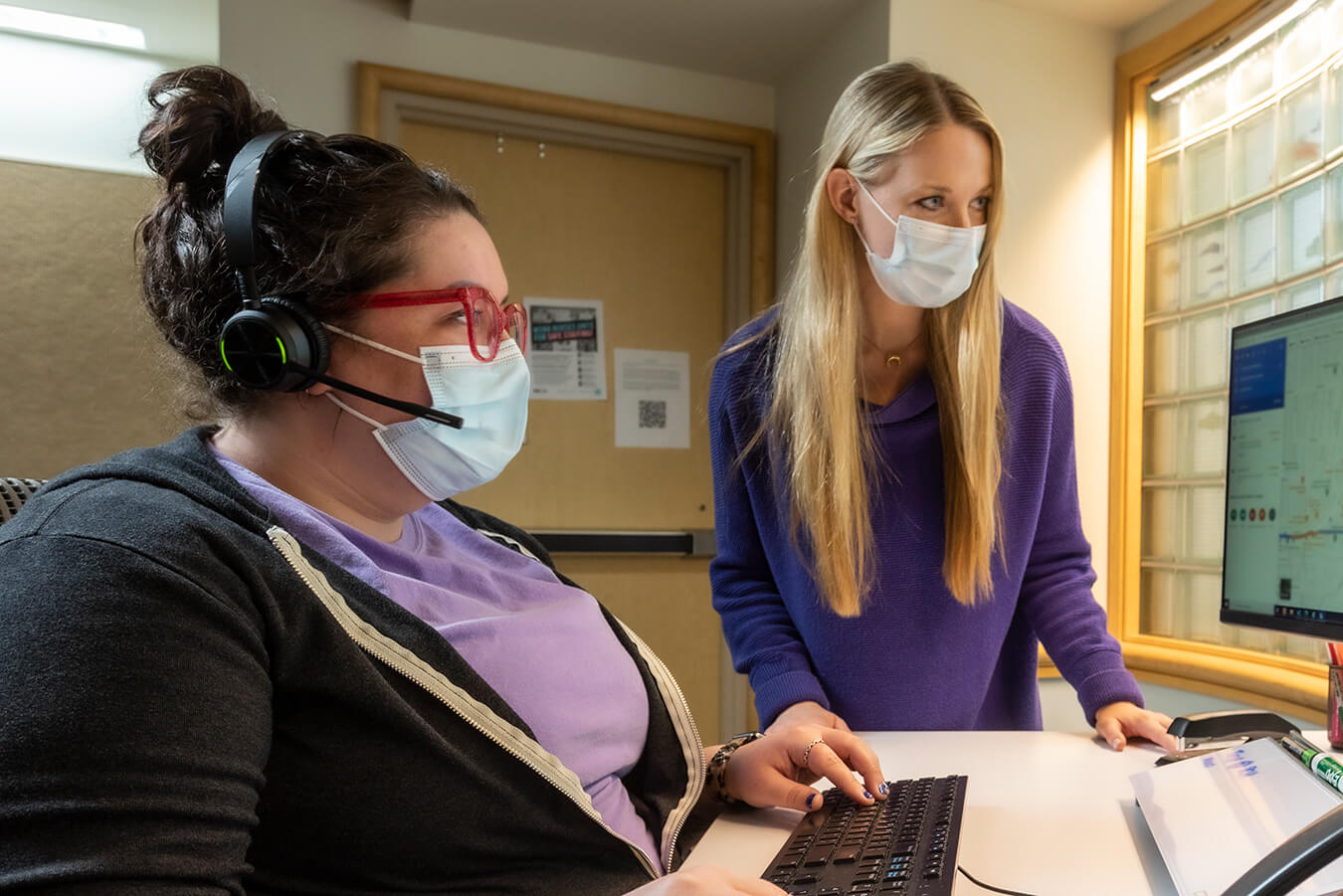 Two nurses in masks looking at a computer screen