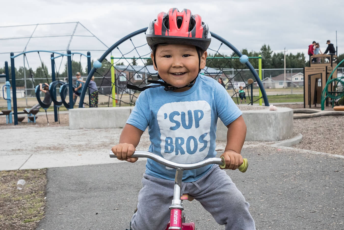 Young boy in blue shirt wearing a red helmet at playground