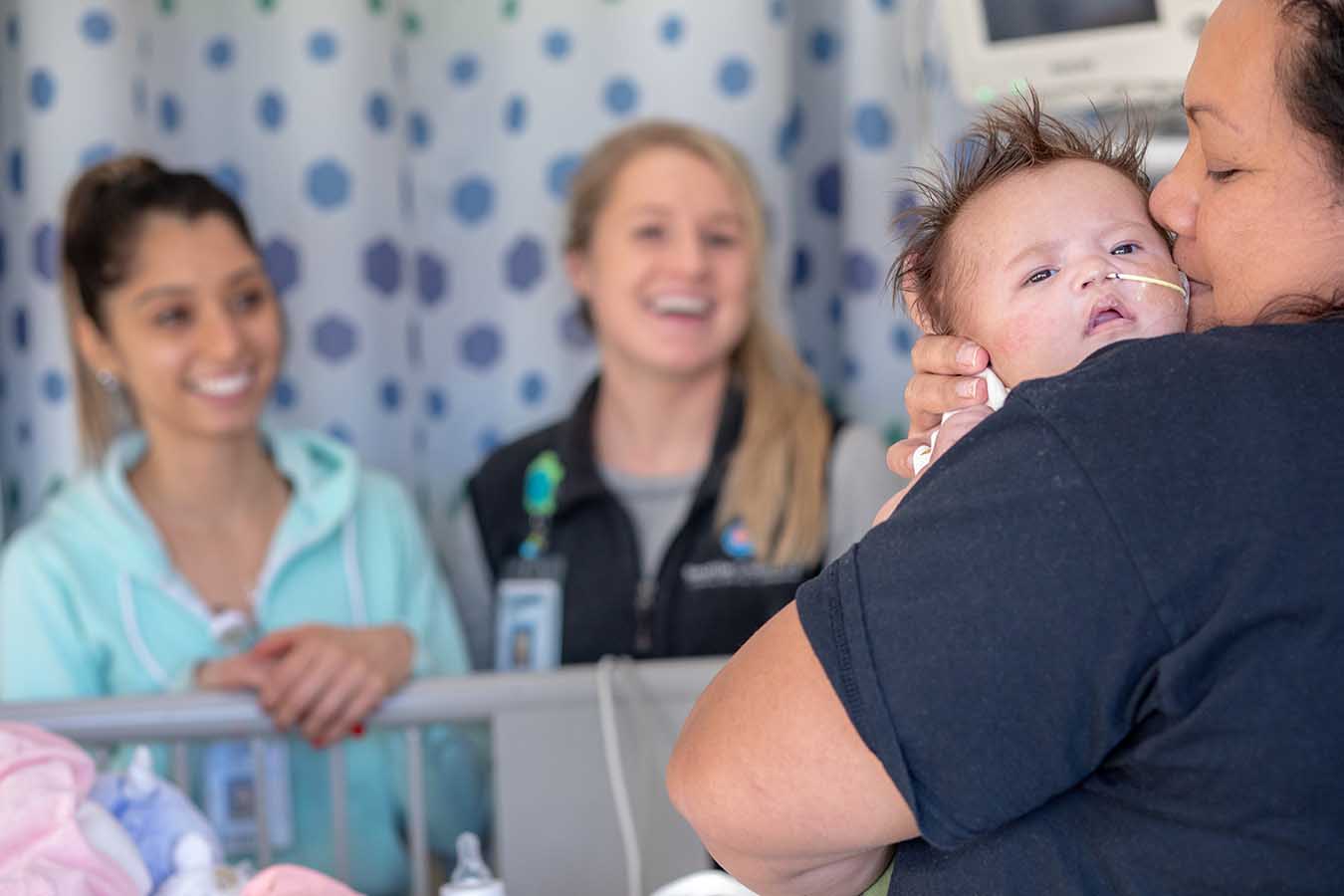 A mother snuggles her baby in front of members of the care team at Seattle Children's