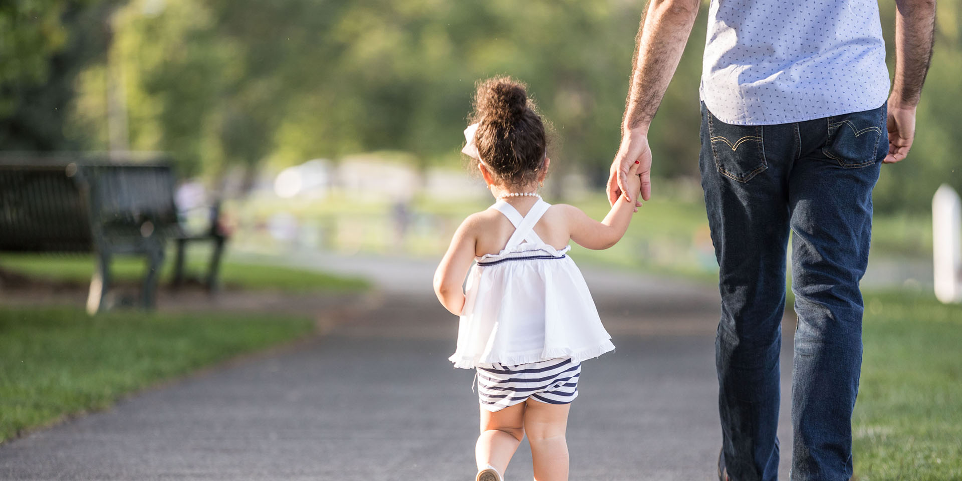 A girl holds her father's hand while walking