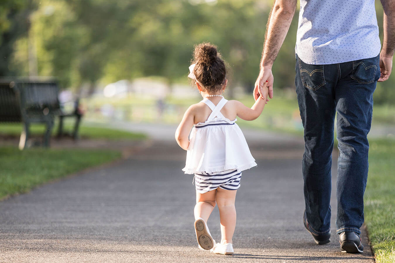 A girl holds her father's hand while walking