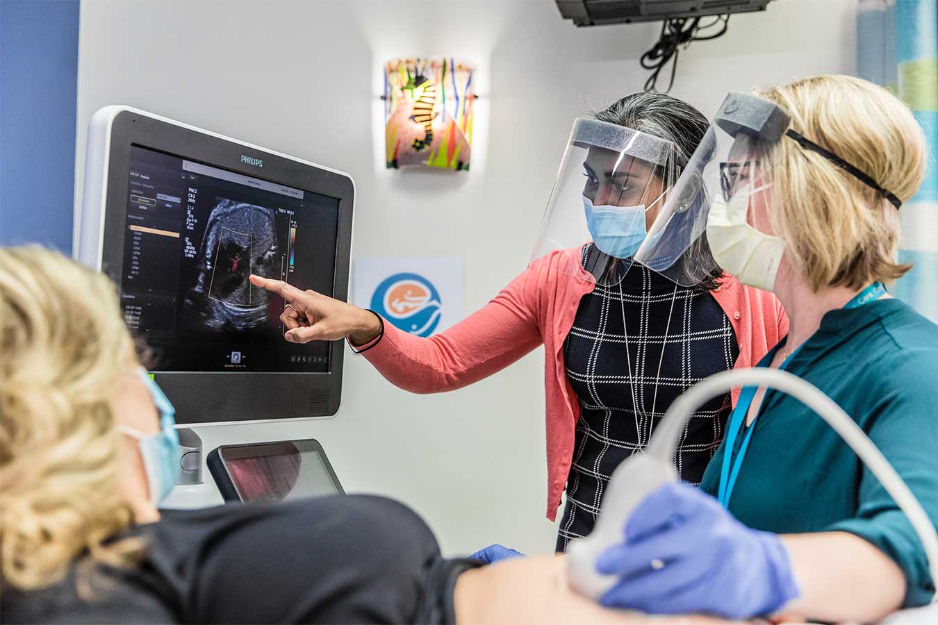 Dr Arya pointing to a ultrasound image with a nurse and patient