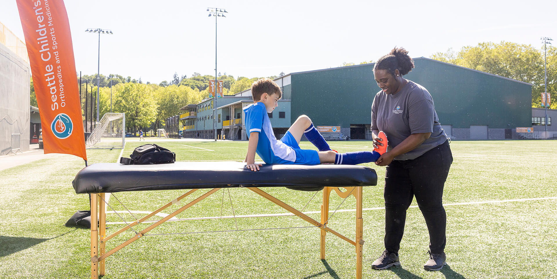 A Seattle Children's athletic trainer evaluates a young soccer player's leg on a sideline treatment table.