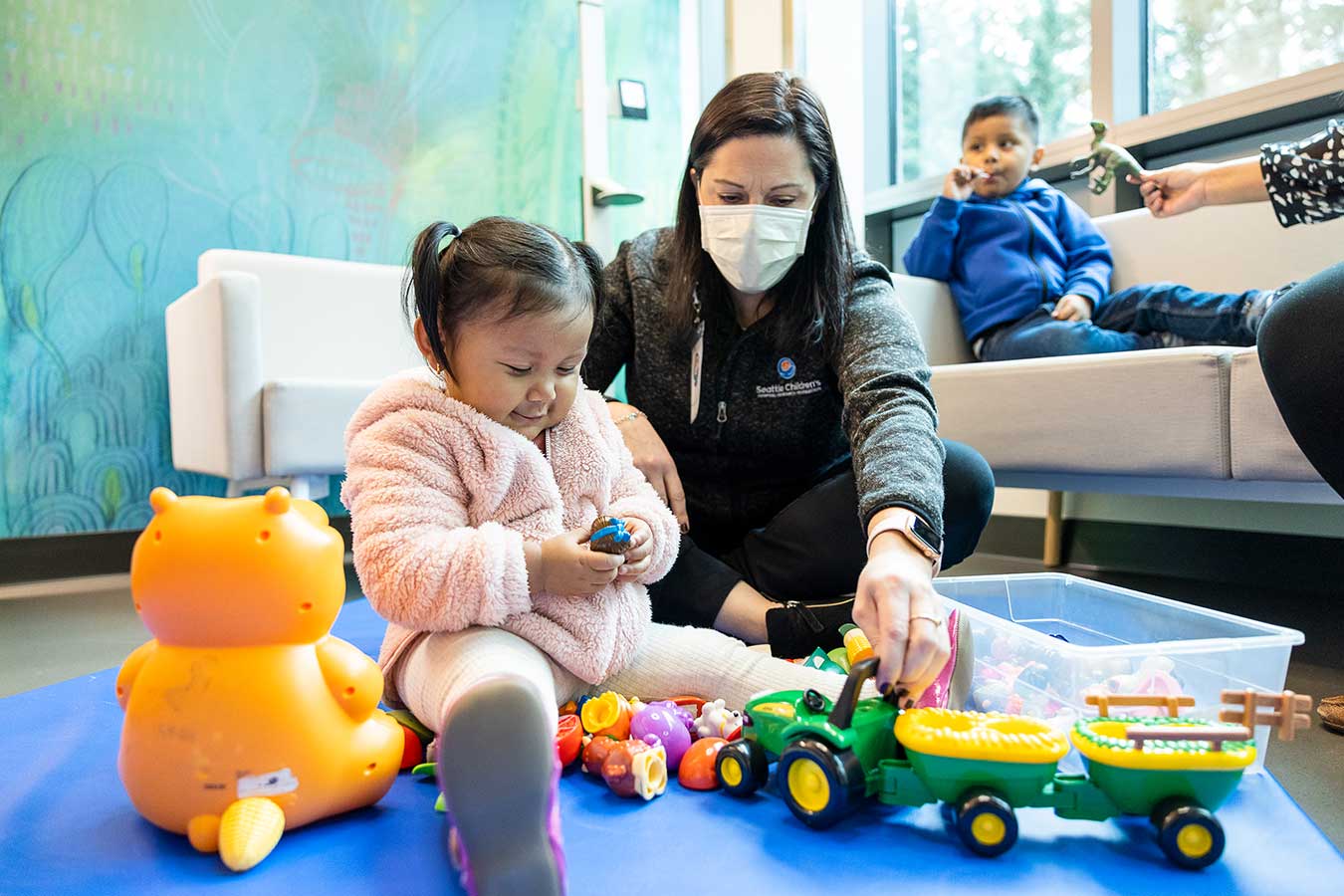 Dr Minjarez sits on the floor with a young child playing with toys