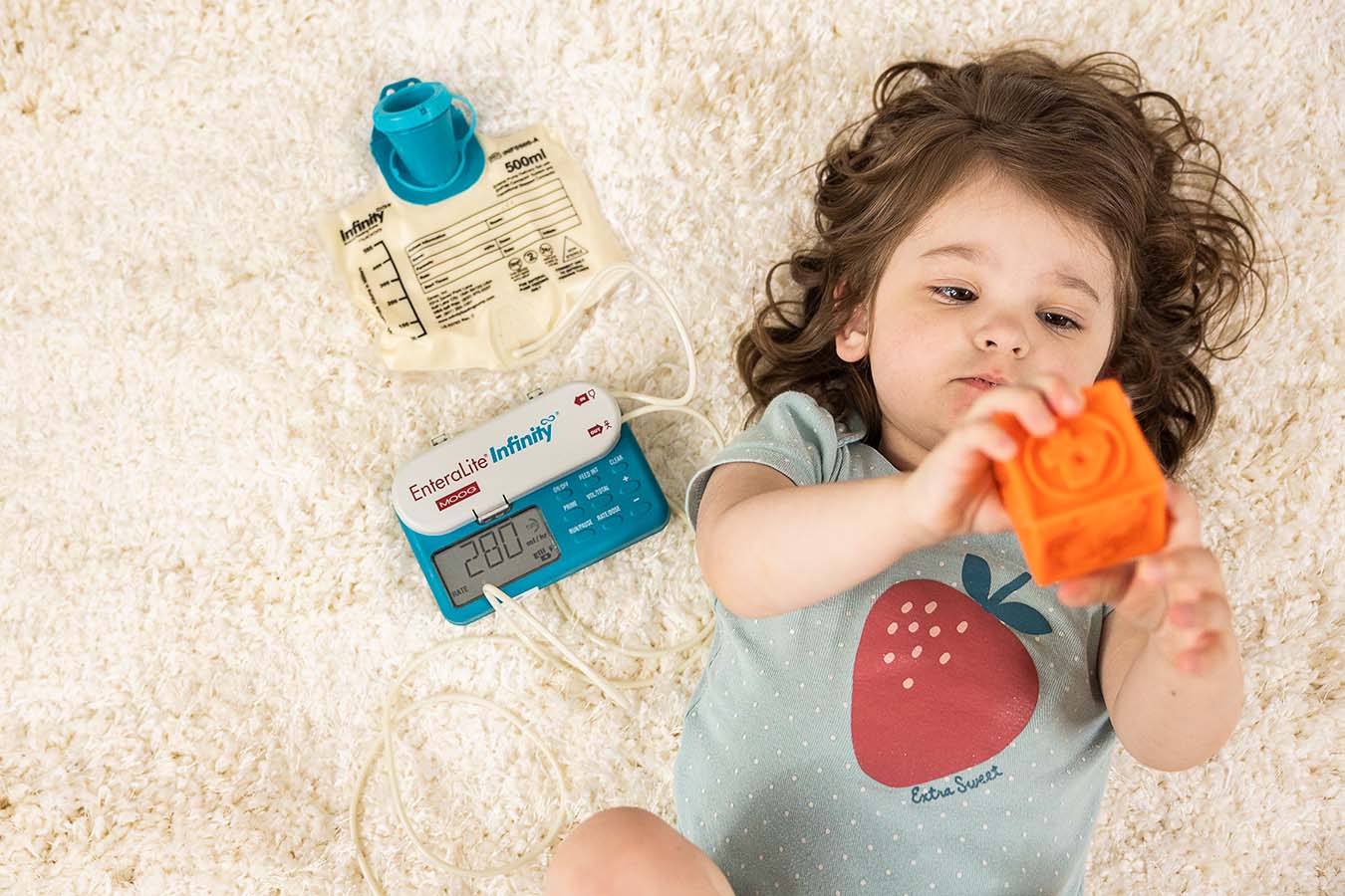 A toddler lays on the ground and plays with a block