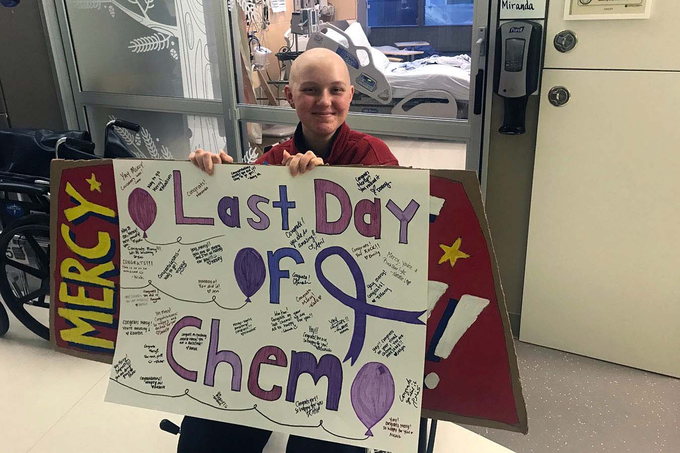 A teenager holds a sign that reads "last day of chemo."