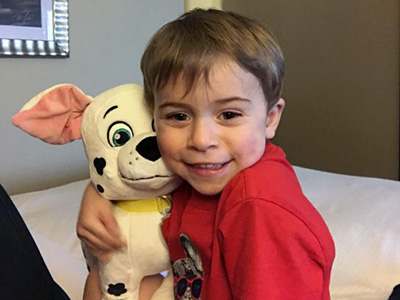 A boy sits on a hospital bed holding a dalmation stuffie