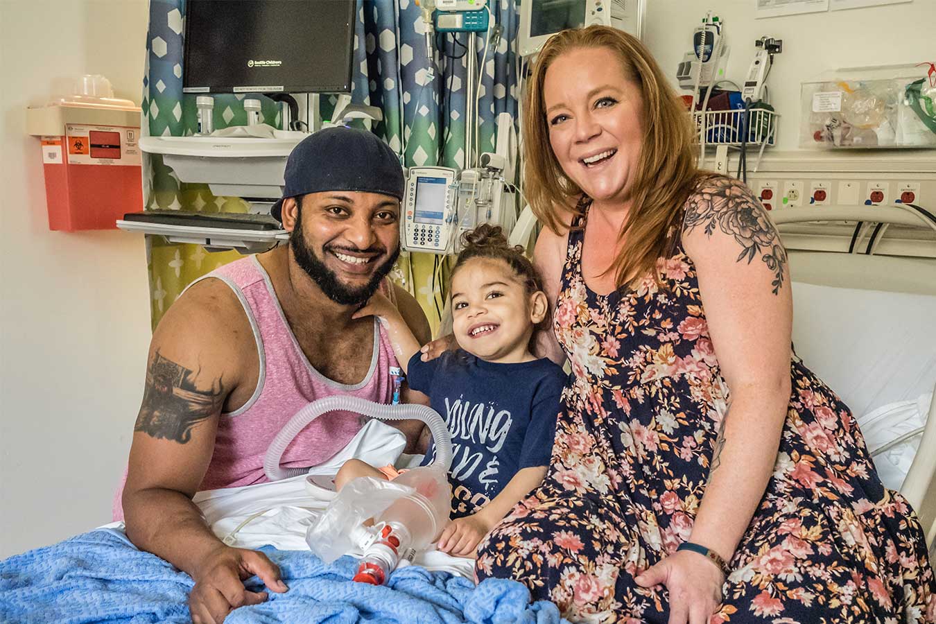 Father, mother, and son sit on hospital bed smiling 