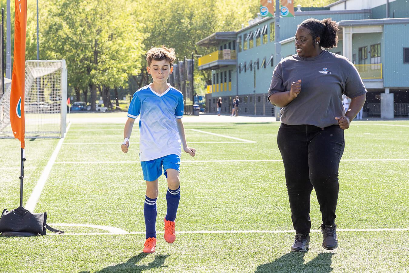 A Seattle Children's sports medicine professional jogs alongside a young soccer player on a turf field to assess his movement.