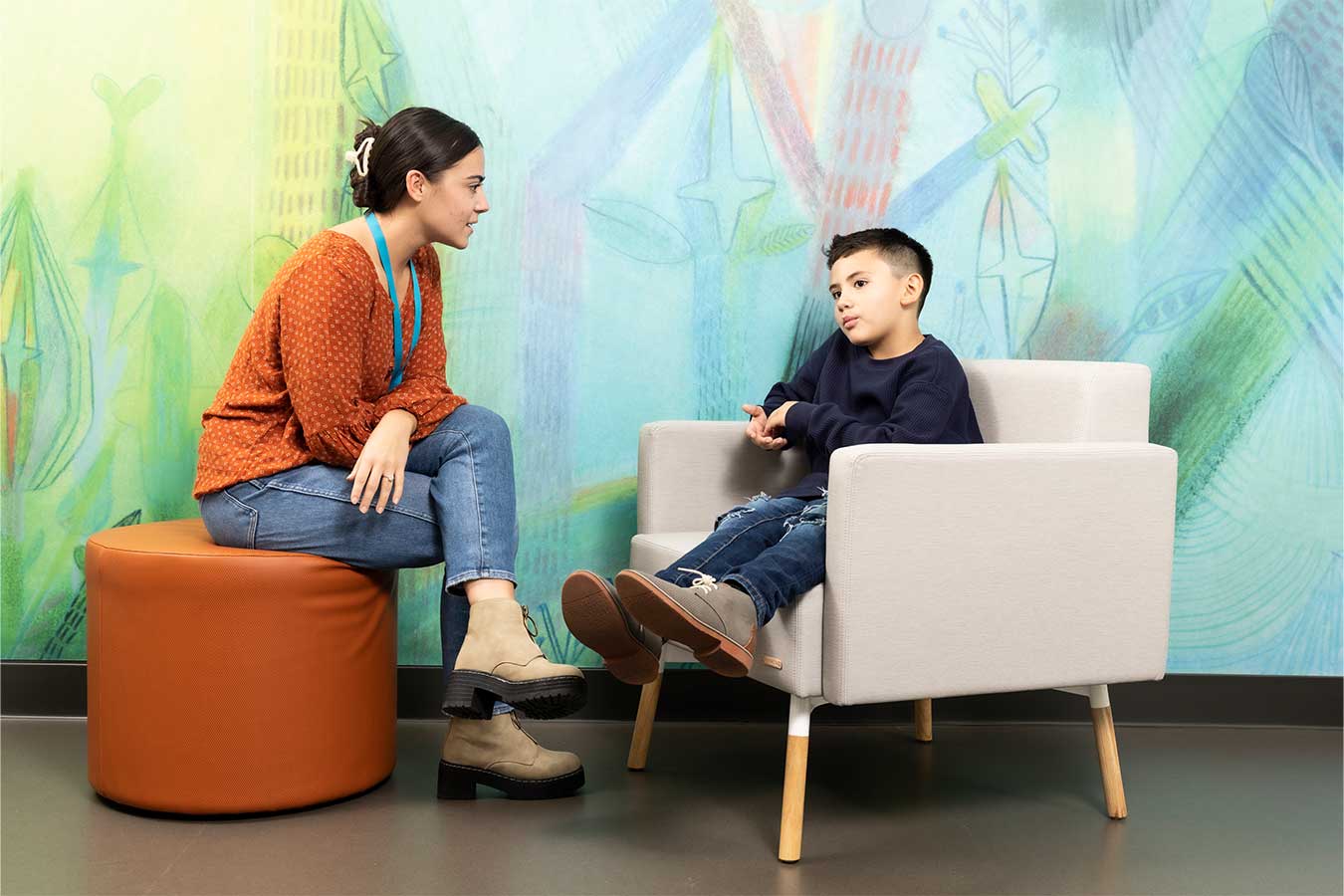 Doctor in orange sweater consults with a young patient in front of a colorful mural wall