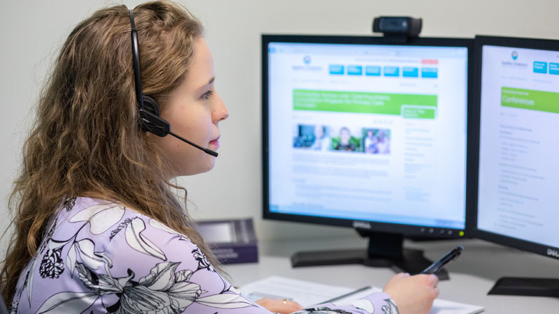 Young woman wearing a headset, looking at dual computer monitors