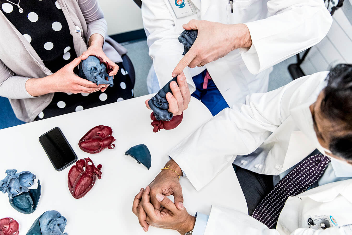Doctors review model hearts at a white table.